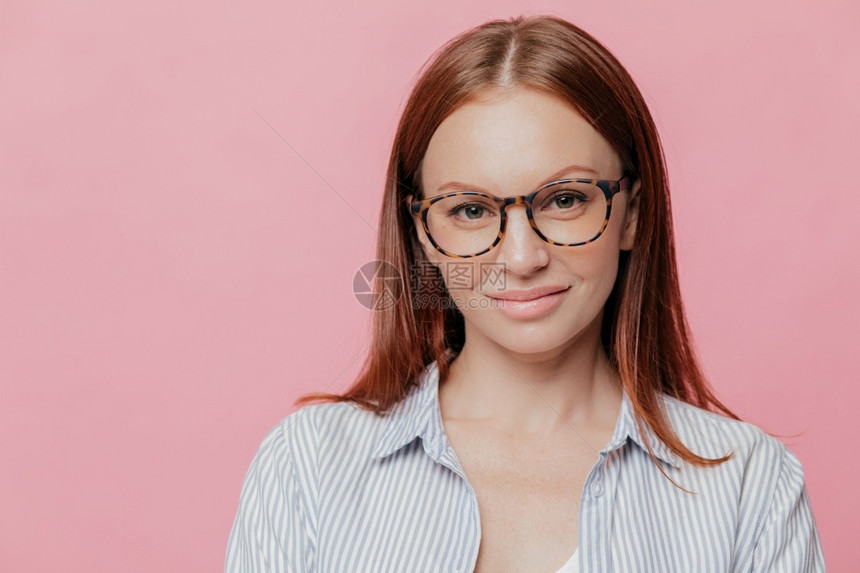 愉快的女记者穿着优雅的衬衫光眼镜满的嘴唇很高兴与人们见面在粉红色工作室墙壁上摆姿势图片