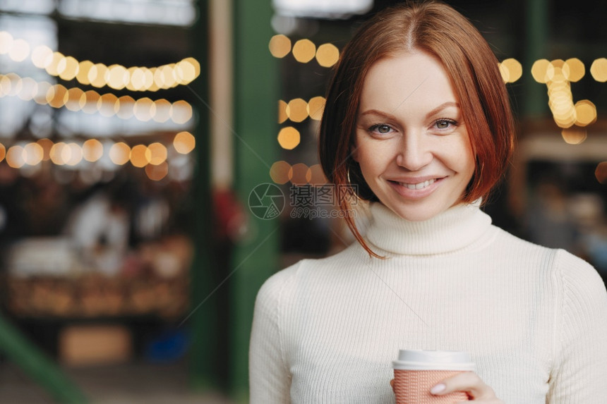 迷人的年轻女形象棕色头发温柔的微笑穿着白领带毛衣拿着纸杯咖啡表达高兴的情图片