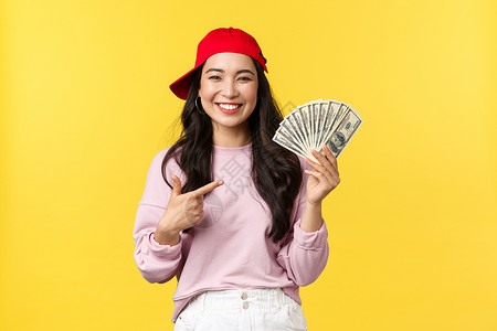满意的年轻女孩知道如何在网上挣钱黄色背景人们的情感生活方式闲暇和美丽概念快乐的20岁女在红帽子上挣钱自豪地点着现金背景图片