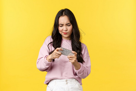 人们的情感生活方式休闲和美丽概念关注和强烈的亚洲女孩试图在移动游戏中度过困难的关卡以自打智能手机屏幕站立黄色背景而眉毛人们的情绪背景图片