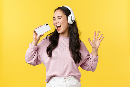人们的情感生活方式闲暇和美观概念在耳机上无忧虑的快乐亚洲女在手机上玩卡拉okap用智能手机作为麦克风唱歌曲人们的情感休闲和美观概背景图片