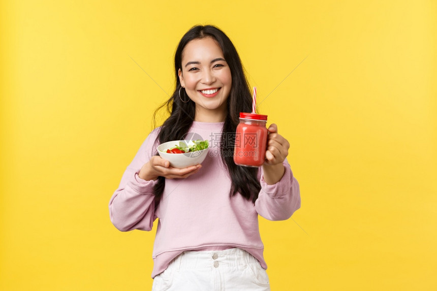 友好和快乐的亚洲女孩伸出手给你拿着沙拉分享午餐一起吃黄色背景人们的情感健康生活方式和食物概念友好和快乐的亚洲女孩伸出手给你黄色背图片