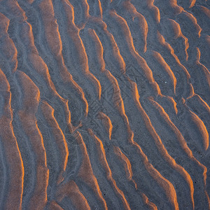 追波风太阳在日落的温暖光照下沙滩上波的抽象模式背景