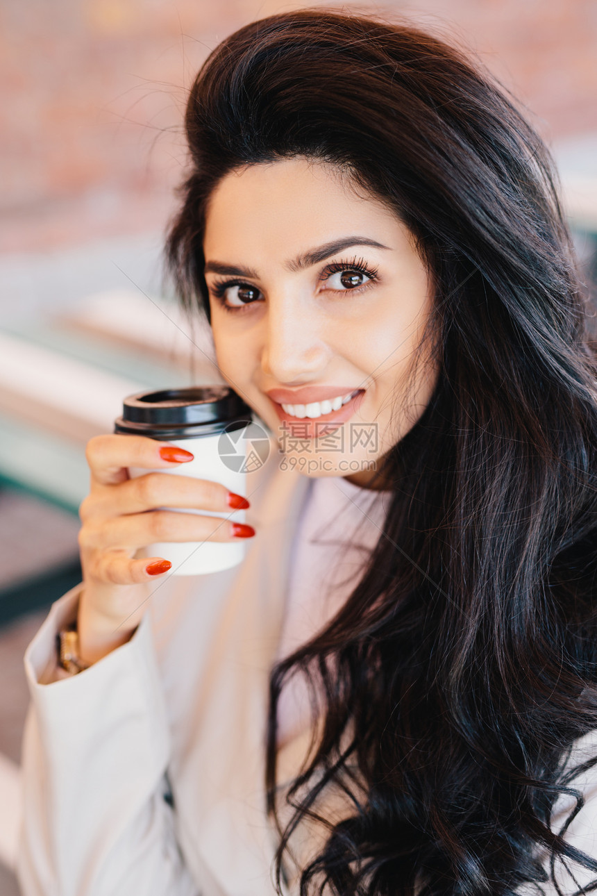 年轻褐色女眉健康皮肤和红指甲将咖啡放在镜头中笑得令人愉快地看图片