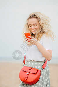 手机外观正面的年轻女使用现代智能手机使用愉快的表达方式在线购物携带明亮的小袋子在海边有户外散步人技术积极的概念背景