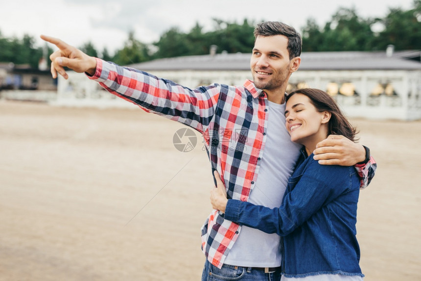 微笑的英俊男人有快乐的表情与妻子共度时光拥抱她露出远处的东西快乐女人感受到丈夫的支持仰着他肩膀闭眼睛女人和男拥抱图片