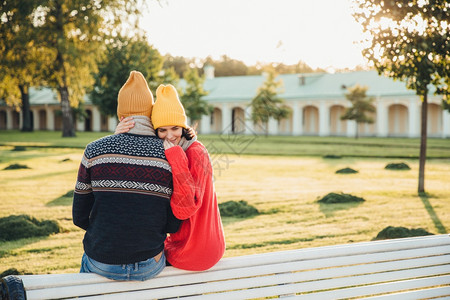 穿着松散的红毛衣美女拥抱着她的男朋友想念他的时间太长了很久前没见过他坐在公园的长凳上聊天愉快欣赏美丽的风景或自然幸福的高清图片素材