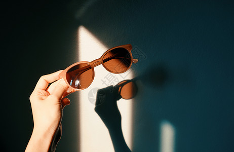 妇女手握着时尚墨镜阳光照耀墙上有阴影潮时和夏季概念图片