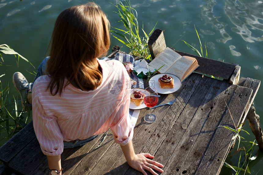 女孩在光亮的夏季河岸木码头上享受野餐图片