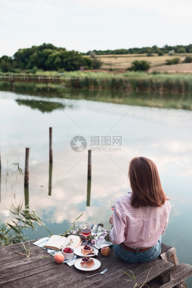 女孩在光亮的夏季河岸木码头上享受野餐图片