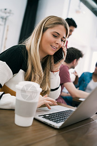 青年商业妇女通过电话交谈在工作场所用笔记本电脑工作图片