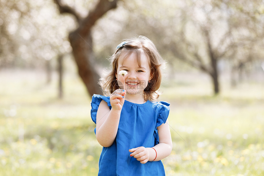 一个可爱的小女孩笑着在蓝色的上衣里玩得开心春花园里有一朵甘菊花个美丽的可爱小女孩笑着在蓝的上衣里玩得开心春花园里有一朵甘菊花图片