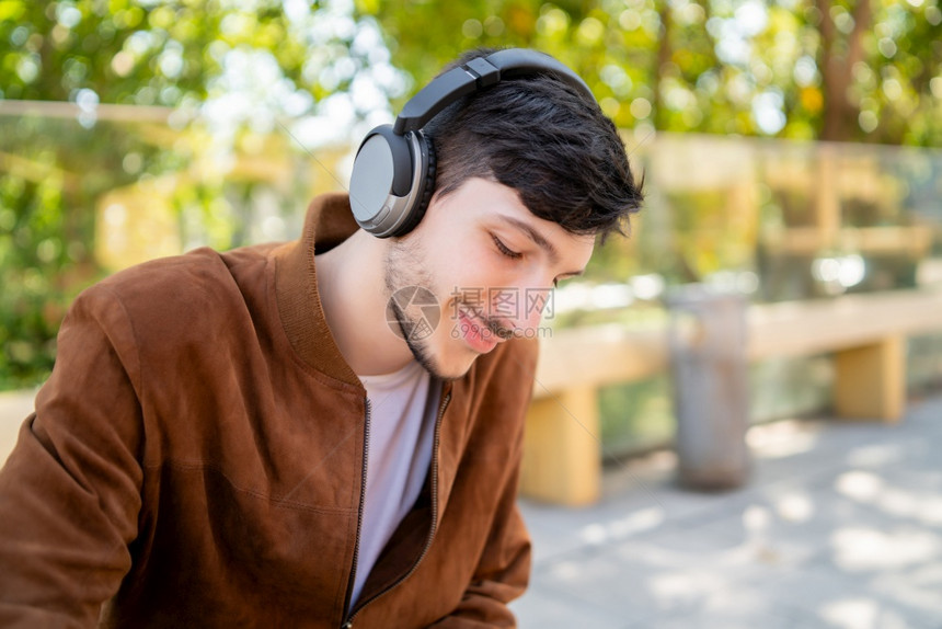 年轻帅哥坐在户外时用耳机听音乐的肖像城市概念图片