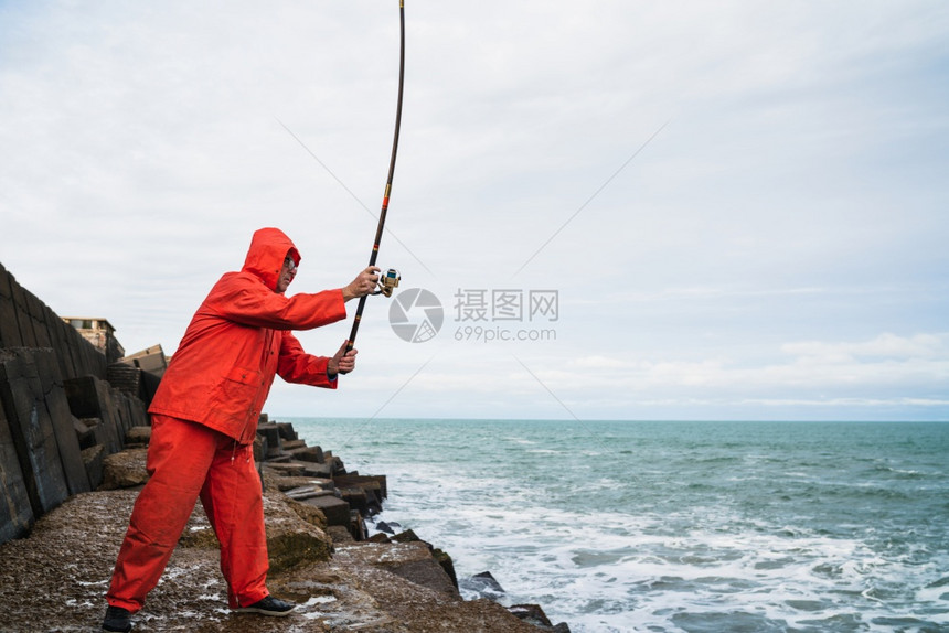 一个老人在海边岩石上钓鱼的肖像概念图片