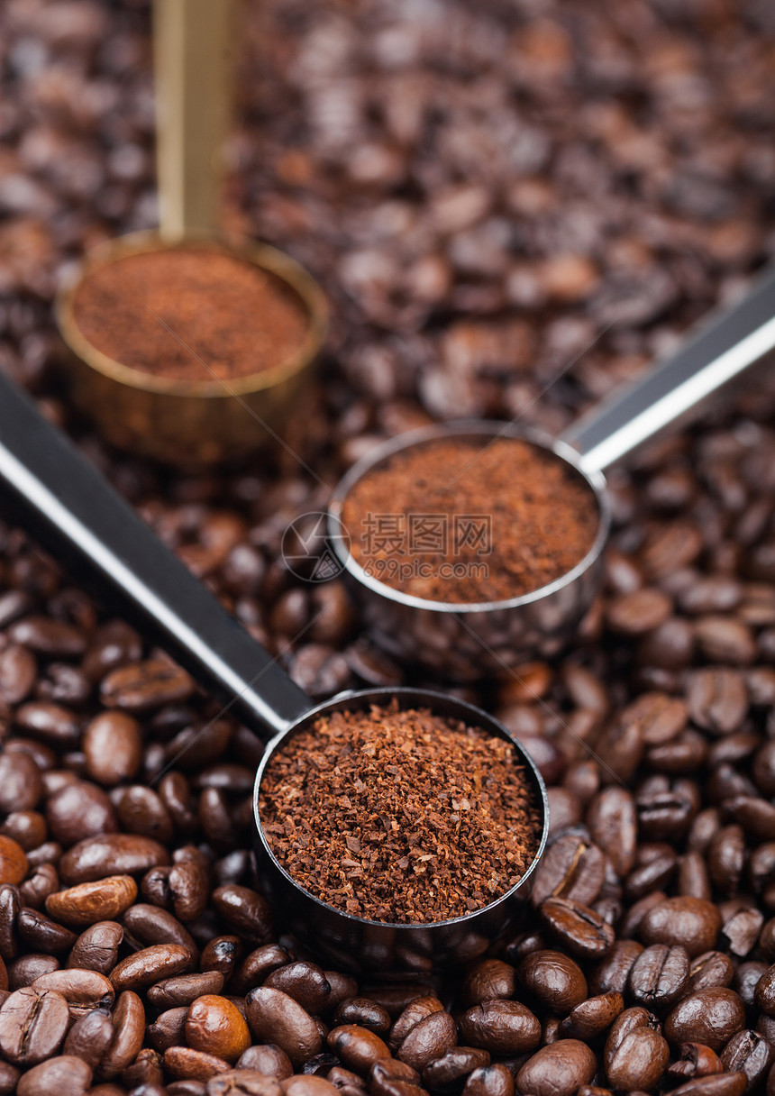 黑银和金钢勺上咖啡豆方的黑银和金钢勺中的新鲜有机咖啡粉图片