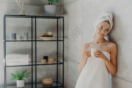 穿着浴巾喝茶或咖啡皮肤干净整洁在灰墙上倾斜美容日SPA和皮肤护理治疗图片