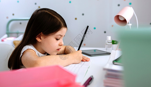 女孩坐在她卧室的桌子上做功课女孩坐在桌子上做功课图片
