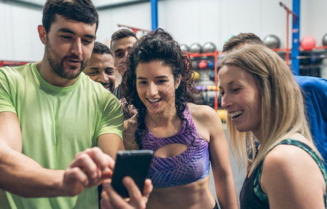 一群运动员笑着看一个健身队友的手机图片