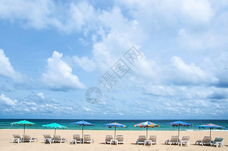 蓝色天空下的绿海白云和多彩的海滩雨伞在布吉的卡塔海滩背景图片