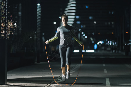 女人跳绳子城市妇女户外运动晚上深夜在城市里图片