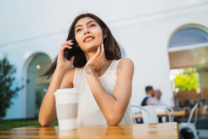 年轻拉丁女人坐在咖啡厅时电话上聊天的肖像图片