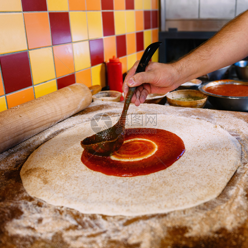 厨师在比萨饼面团上撒番茄酱披萨餐厅的金属拉链披萨制作过程图片