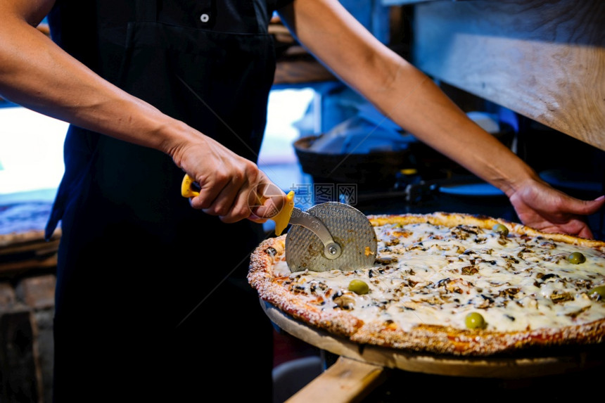 身穿黑色制服的女厨师穿着披萨和木皮上的披萨卷切刀图片