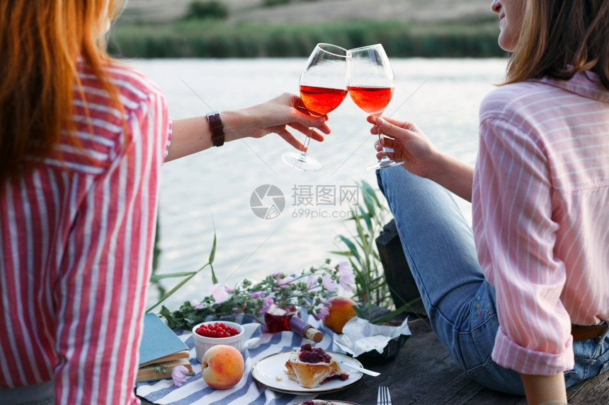 两个女孩在光亮的夏季河岸木码头上享受野餐图片