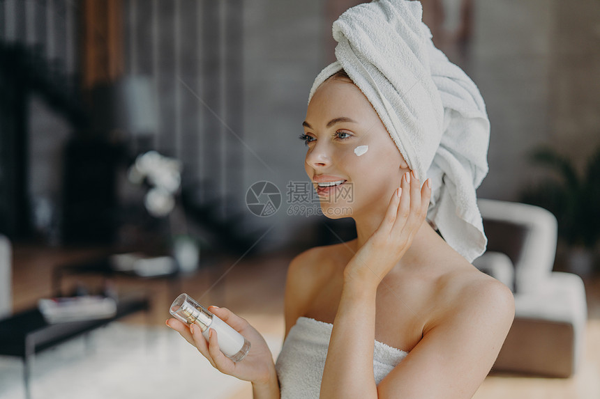 穿着白浴巾的美丽欧洲年轻女子头部涂白浴巾施用面霜和体液洗完澡后享受皮肤护理程序单独在家化妆图片
