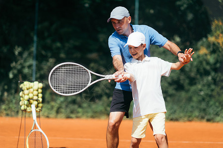 在粘土场上与网球教官一起训练男孩在网球场上训练男孩背景图片