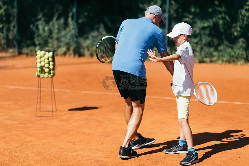 网球教练在粘土场上有年轻才华男孩有网球课图片
