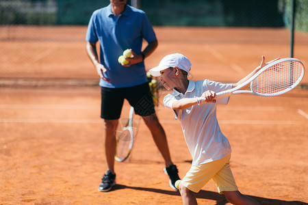 在粘土场上有年轻才华的网球教官有课的男孩在粘土场上与年青男孩一起的网球教官背景图片