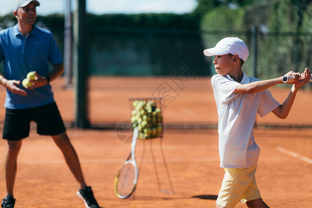 与男孩和教练一起上网球课的教练和男孩在粘土法庭上网球课的男孩教练图片