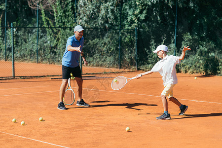 网球教官男孩在粘土场上有网球课教官和男孩在网球课上有教官背景图片