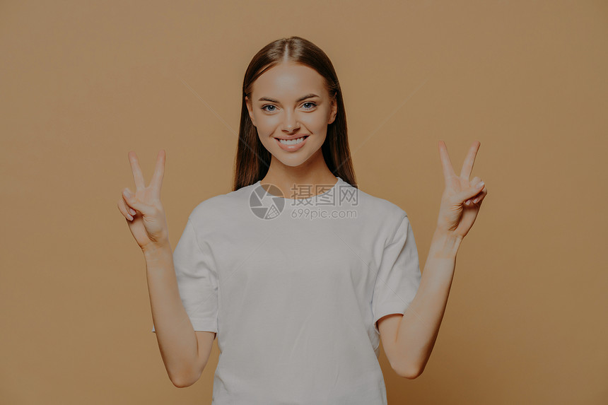 欢乐观的年轻causin女士举起手来展示和平姿态用手指显示和平姿态胜利标志表示二号图片