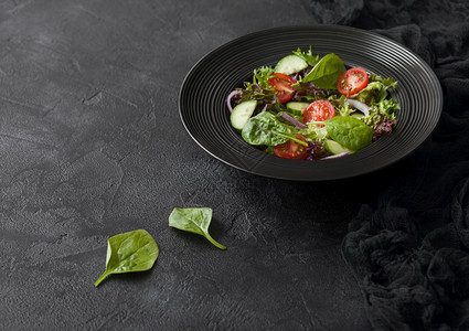 健康新鲜蔬菜沙拉有生和西红柿洋葱和黑碗菠菜桌背景图片