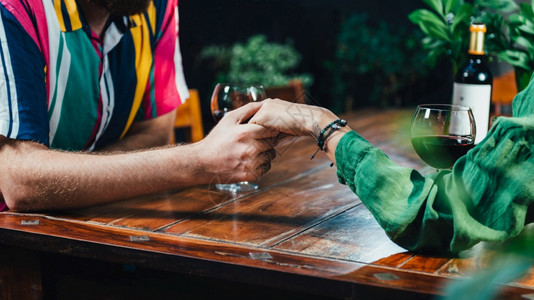 一对夫妇手牵在餐馆喝红酒一对夫妇坐在木桌旁穿着多彩的服装装备高清图片素材
