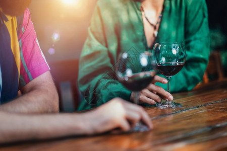 一对夫妇在木制餐厅桌边喝红酒穿着多彩的服装不规则剪裁高清图片素材