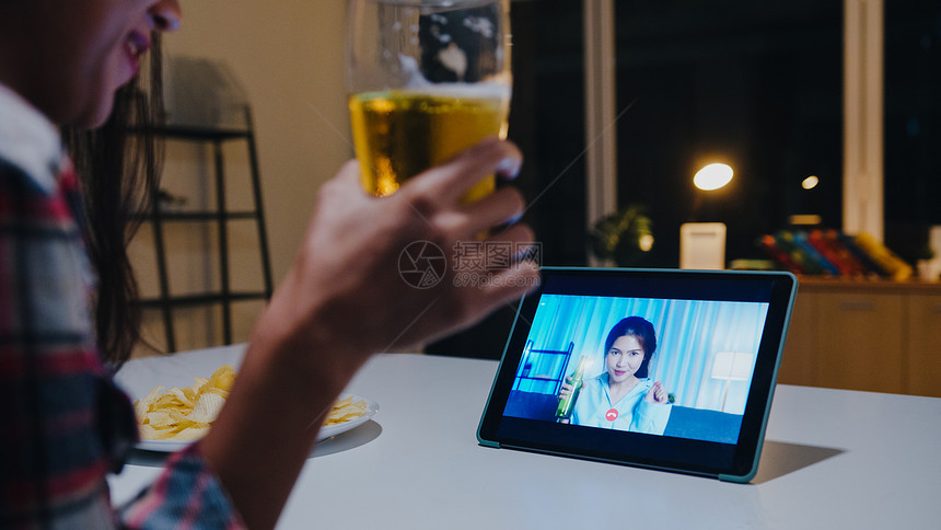 喝啤酒的年青女士享受欢乐的瞬间晚宴活动在线庆祝通过视频电话在家中的客厅晚上社交消遣图片