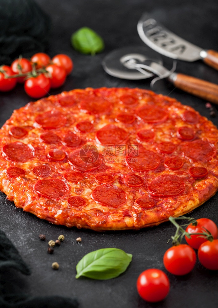 鲜烤热辣披萨配有切轮刀和子配有西红柿和黑餐桌底的烤肉图片