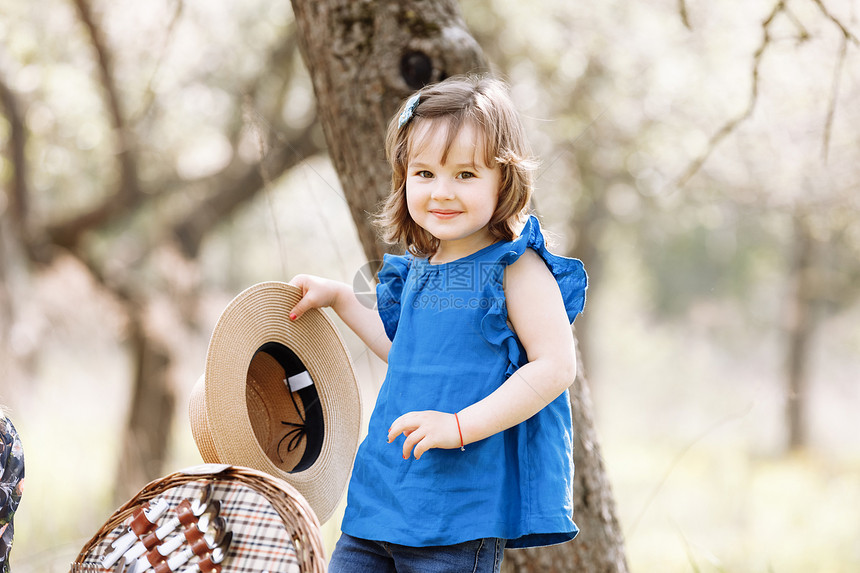 可爱的小女孩笑着穿蓝色的上衣戴着妈的帽子在春天花园里美丽可爱小女孩笑着穿妈的帽子图片
