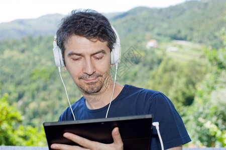 青年男子在户外持有带耳机的平板电脑背景图片