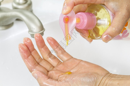 女用手从瓶中液洗肥皂与浴室水槽和背景龙头一起用液洗肥皂的横向照片图片