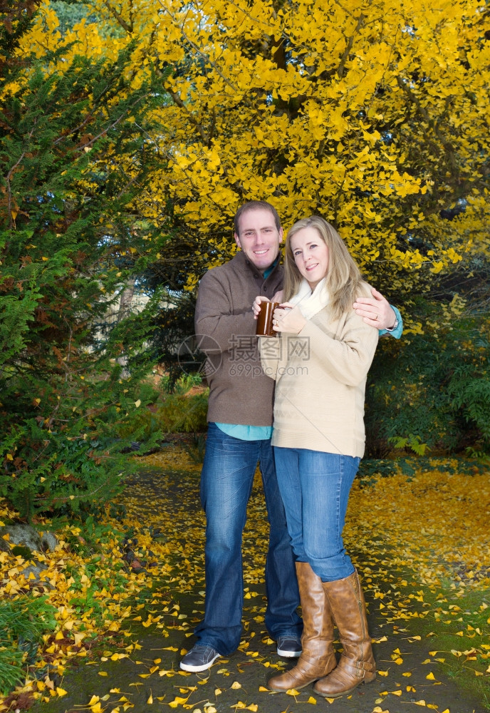 垂直照片显示成年夫妇在公园一个愉快的秋天一起喝杯咖啡时相互拥抱的垂直照片图片