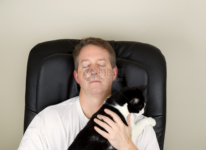 照片显示成年男子穿着白衬衫在按摩椅上放松眼睛闭着手握黑白家庭猫图片