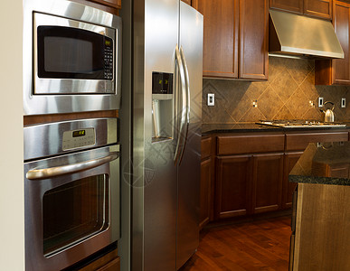 现代住宅厨房不锈钢器件的近照片上面有石质柜顶樱桃木子有硬地板背景图片