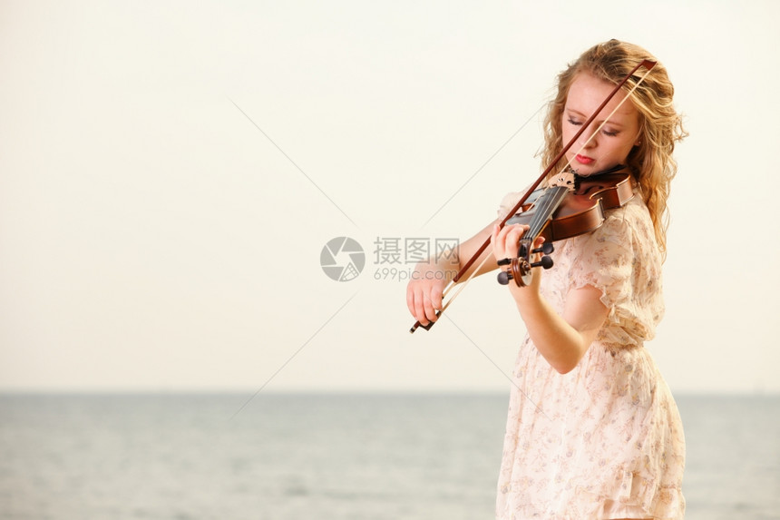 海滩上玩小提琴的金发女孩音乐爱好者的概念图片