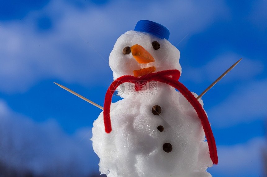 圣诞小雪人穿着蓝螺丝顶的戴红色帽子围巾露天有牙签冬季节蓝天空背景图片