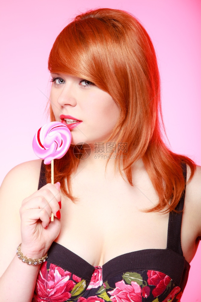 拿着糖果的感年轻女人红头发孩在粉色上吃甜的棒糖演播室拍的甜图片