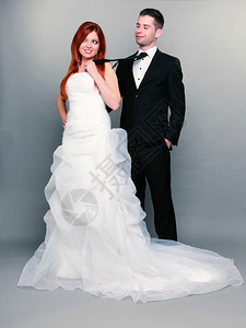 结婚日幸福的已夫妇红发新娘和郎的肖像女人拉着男的领带工作室拍着灰色的背景牵引高清图片素材